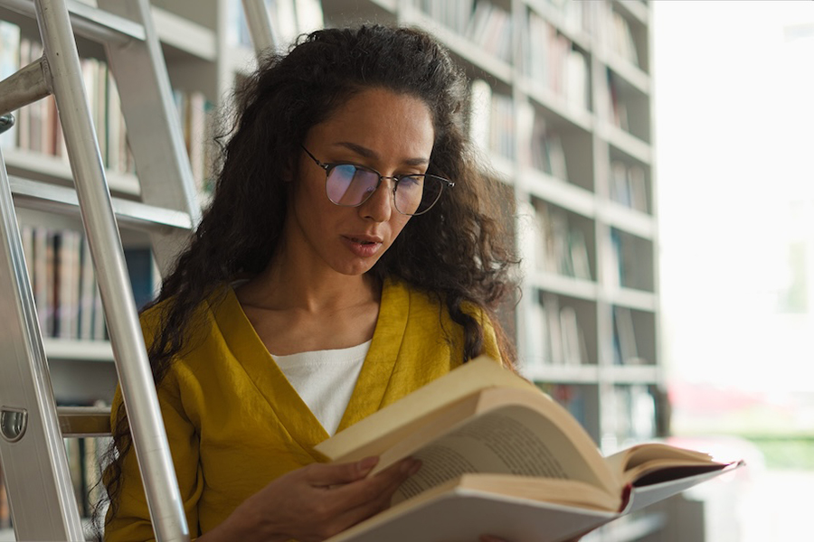 Latino Arabian woman librarian worker library ladder bookshelves textbooks knowledge education research turning pages holding book girl read bookworm reader teacher university learning study archive
